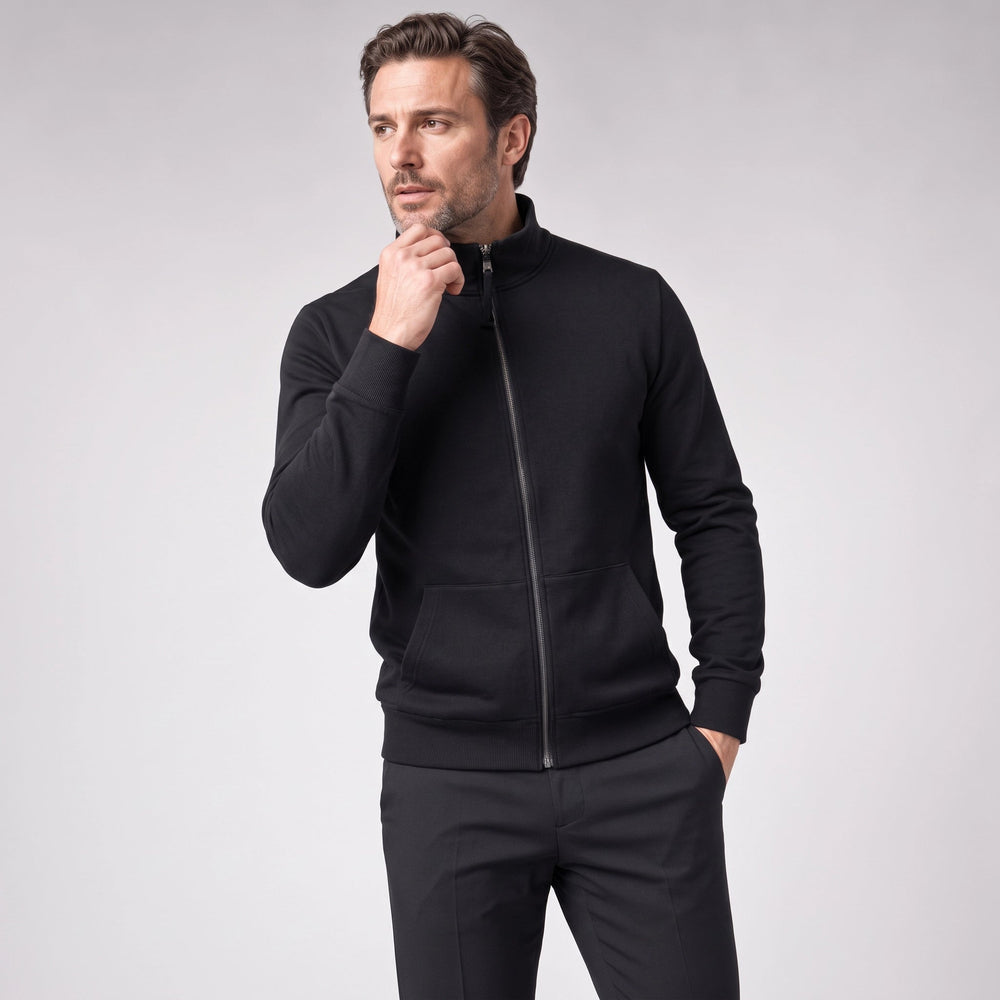 Man wearing a black zip-up sweatshirt with black trousers, one hand raised to his chin | Chaps London