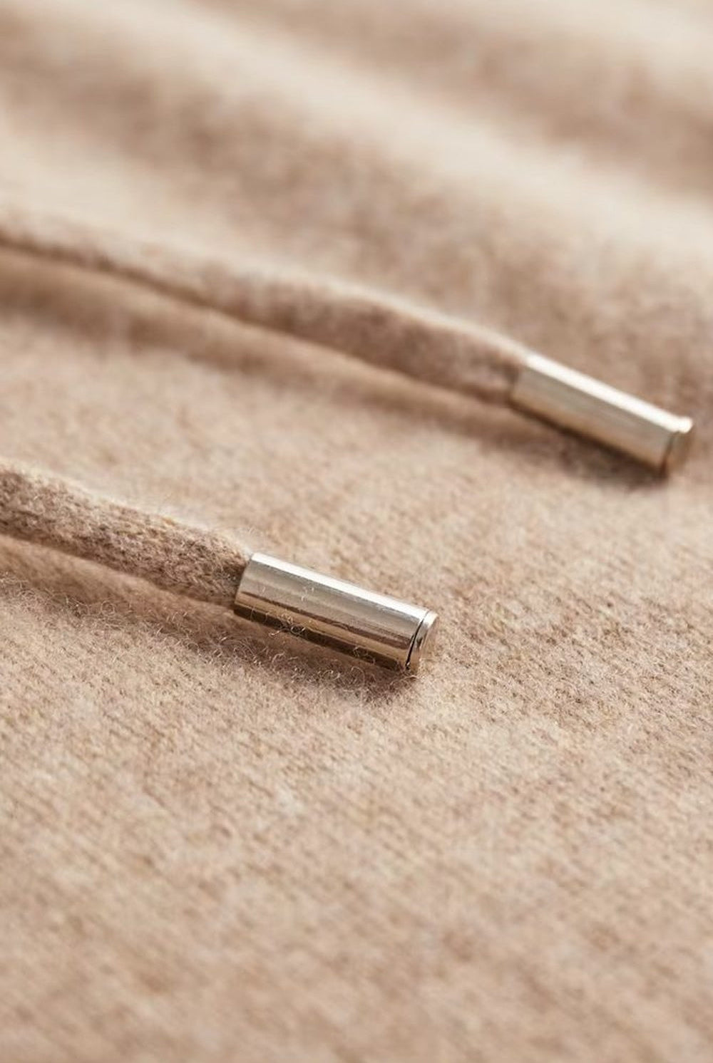 Men's knitted hooded jumper in beige, close-up of the metal tips of the drawstring