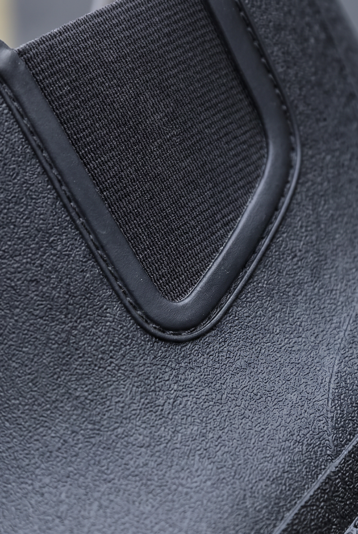 A pair of black rubber Chelsea style rain boots with elastic side panels and pull tabs standing on a street with yellow road markings, close-up view