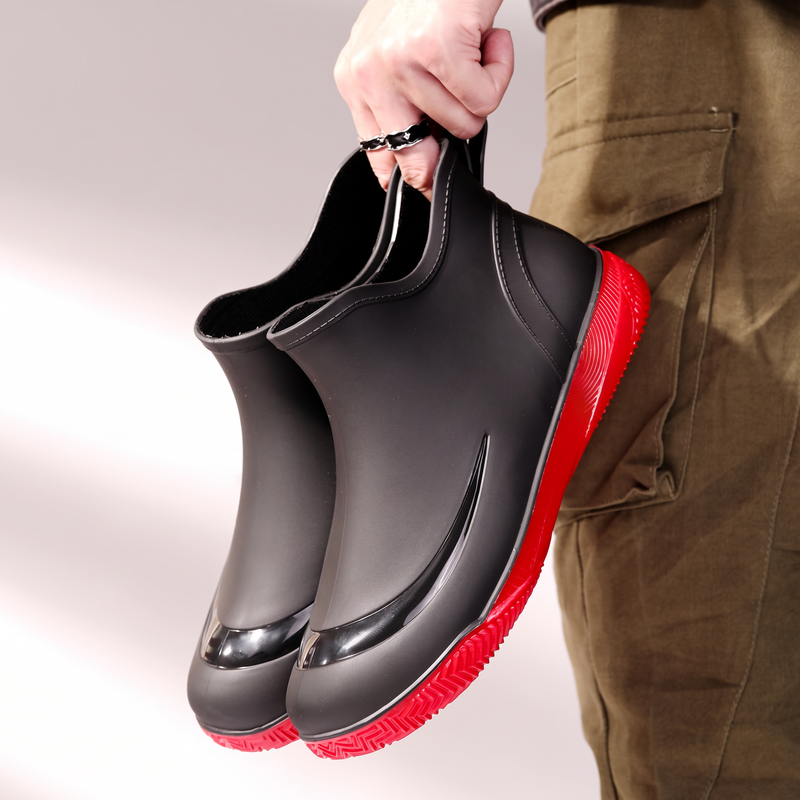 Hand holding a pair of black wellies with red soles, side view