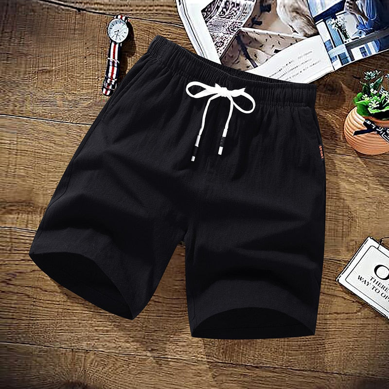 Black cotton drawstring shorts laid flat on wooden surface with accessories | Chaps London