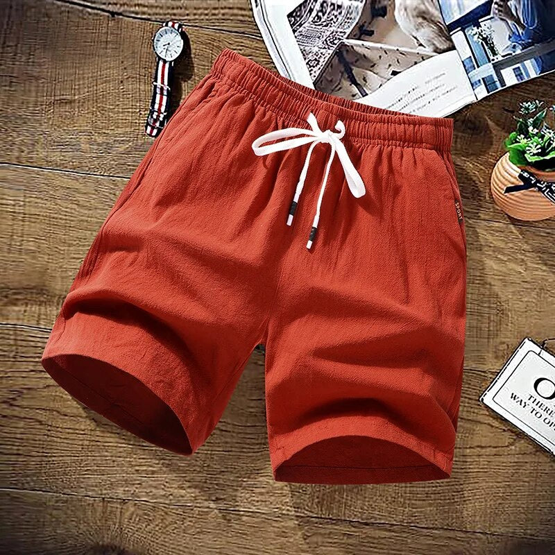 Orange cotton drawstring shorts folded flat on wooden surface with accessories | Chaps London