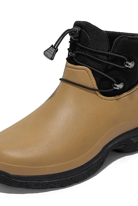 Three quarter studio view of a tan rubber ankle rain boot with a black fabric collar, elastic toggle lacing, a pull tab and a chunky black textured sole on a white background.