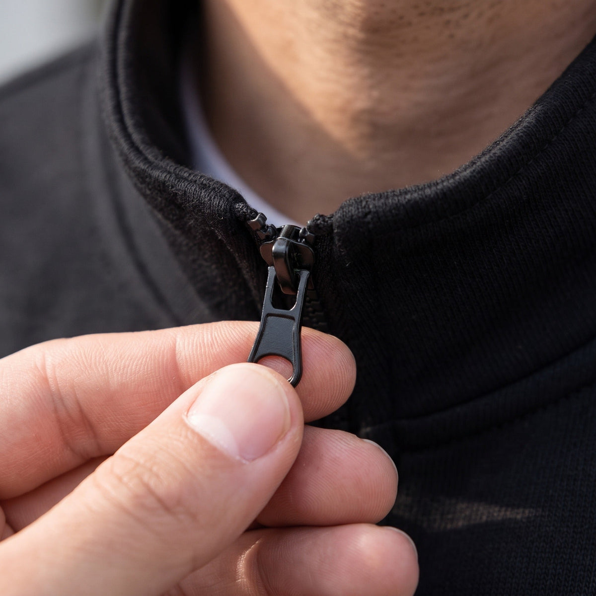 Black stand collar zip jacket close-up, worn by person, hand on zipper | Chaps London