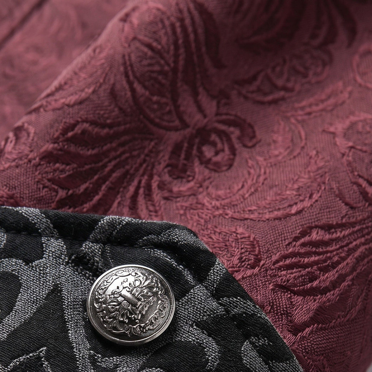 Burgundy jacquard fabric with ornate pattern beside black textured fabric and silver button | Chaps London