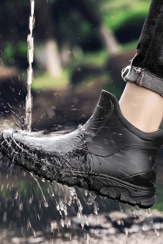 A black rain boot being splashed with a stream of water, worn on a leg with rolled black jeans.
