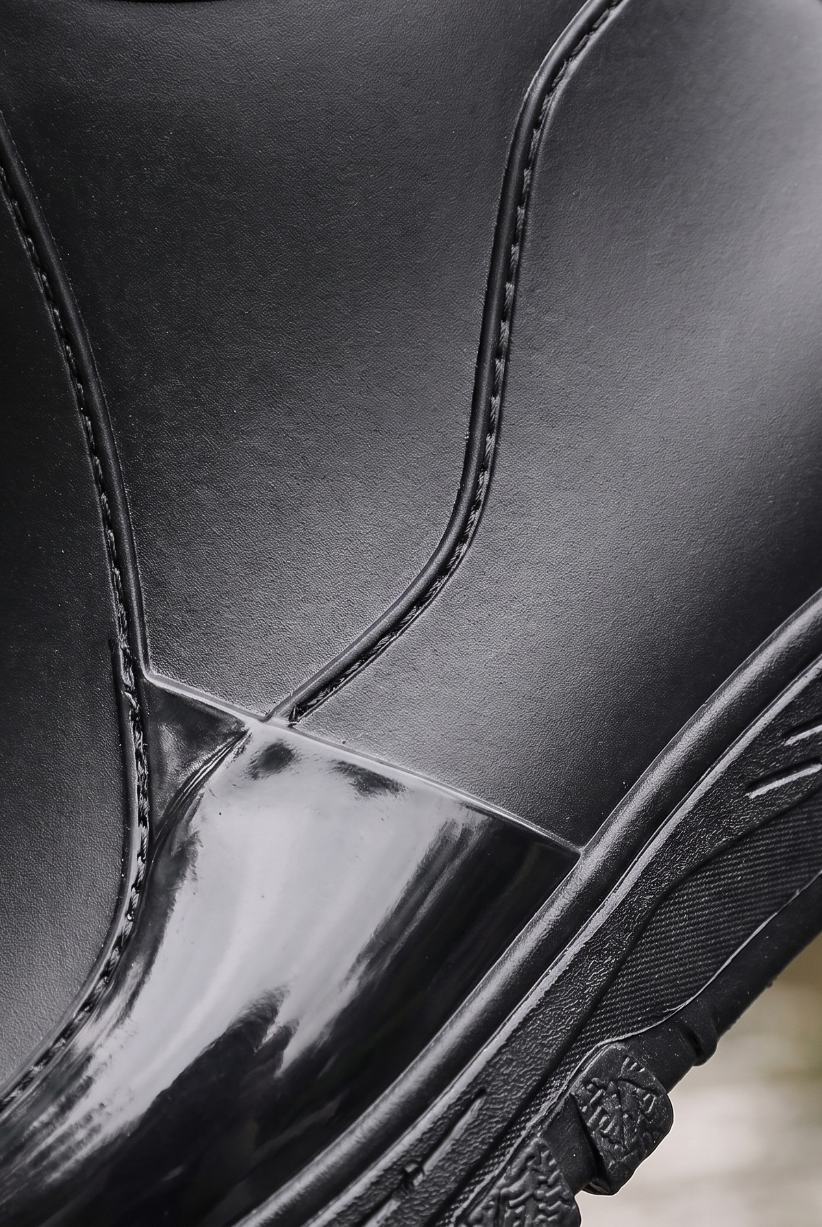 A black rain boot being splashed with a stream of water, worn on a leg with rolled black jeans, close-up view