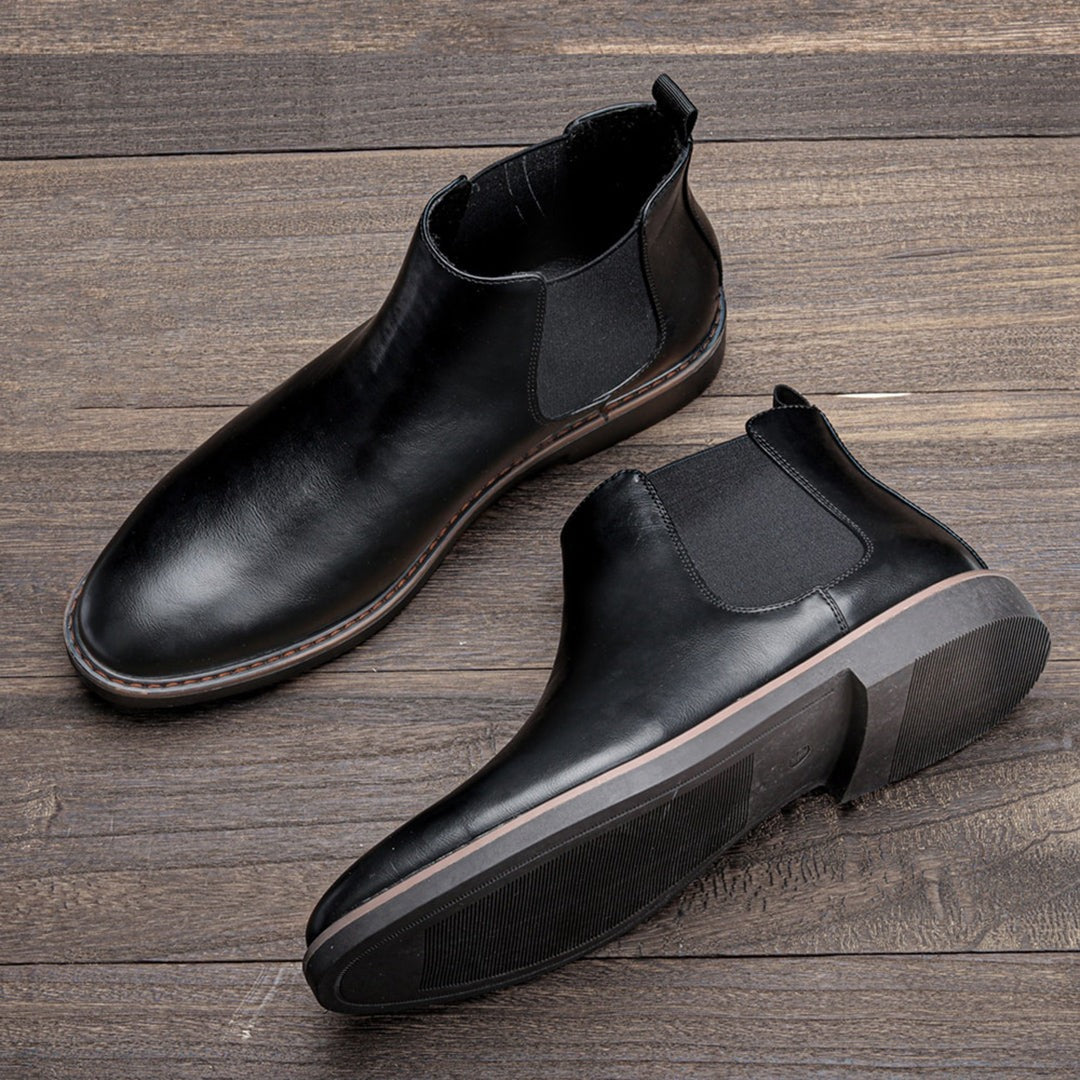 Black leather Chelsea boots with elastic side panels, shown flat on wood | Chaps London