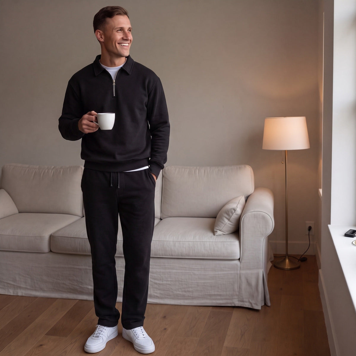 Man wearing black quarter zip sweatshirt and joggers, holding coffee mug indoors | Chaps London