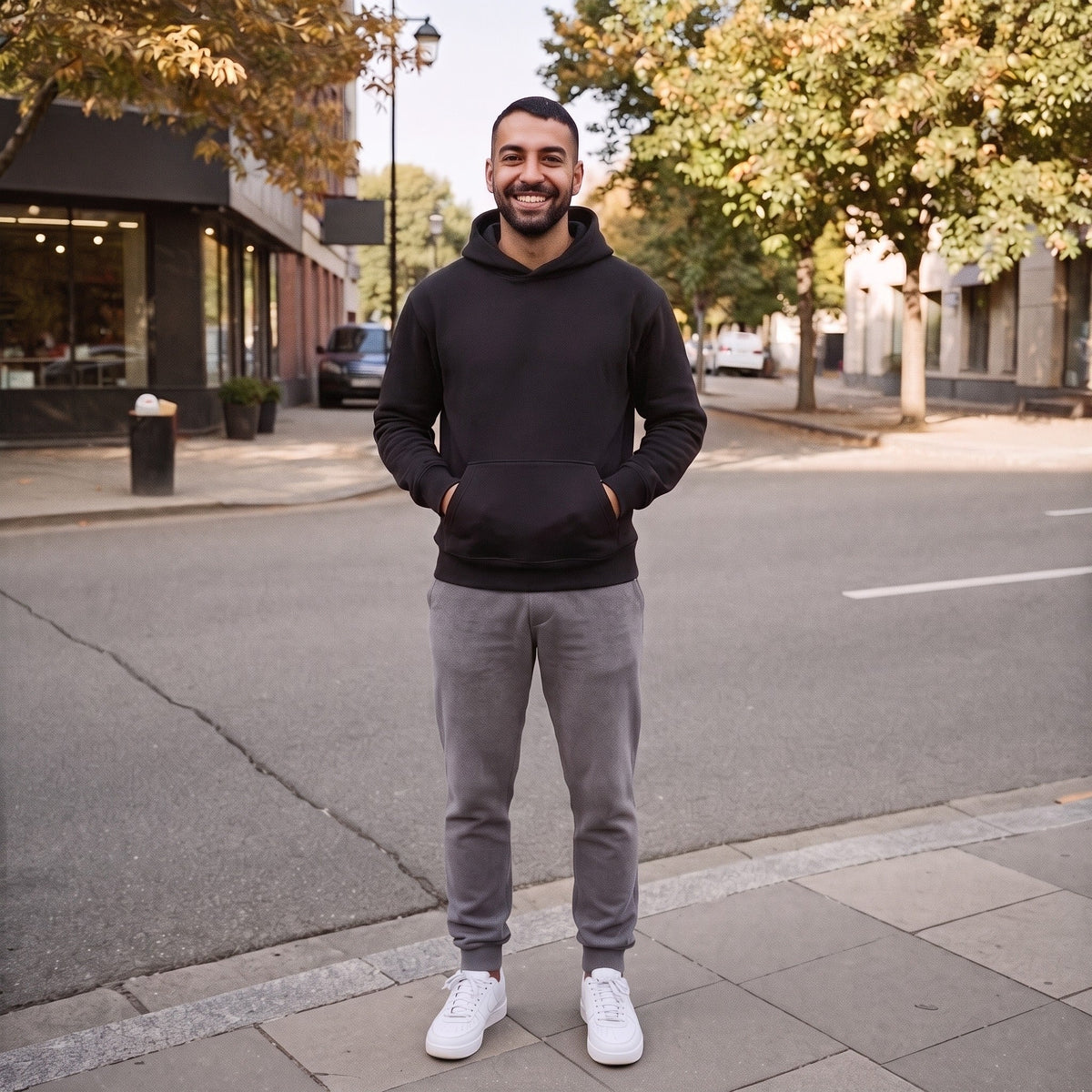 Man wearing black pullover hoodie and grey joggers, standing outdoors on street | Chaps London