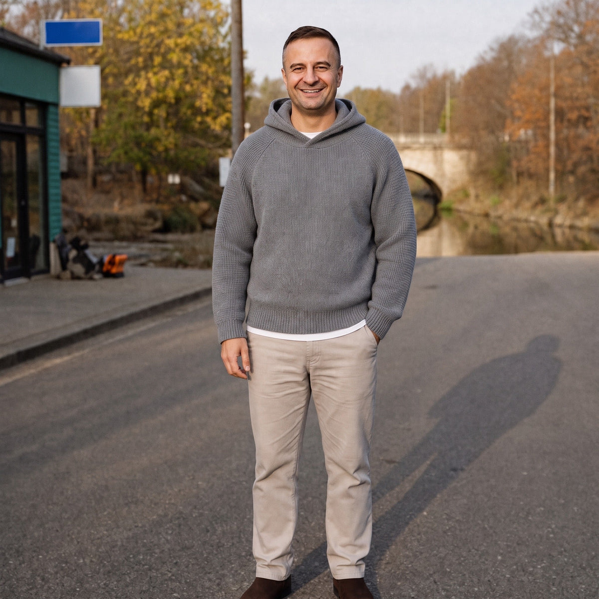 Man wearing grey knit hoodie with beige pants, standing outdoors on road | Chaps London