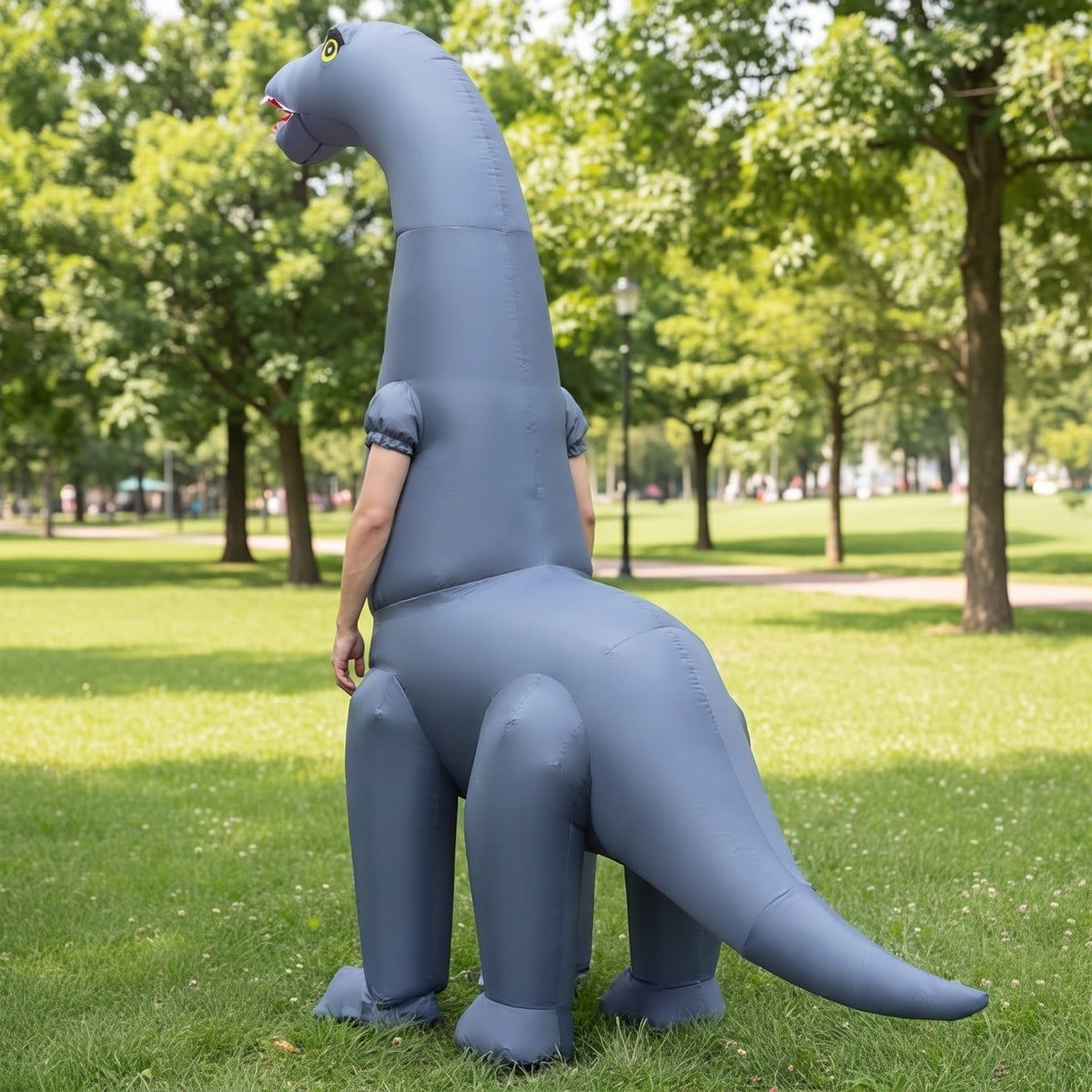 Gray inflatable long-neck dinosaur costume worn by person standing outdoors on grass | Chaps London