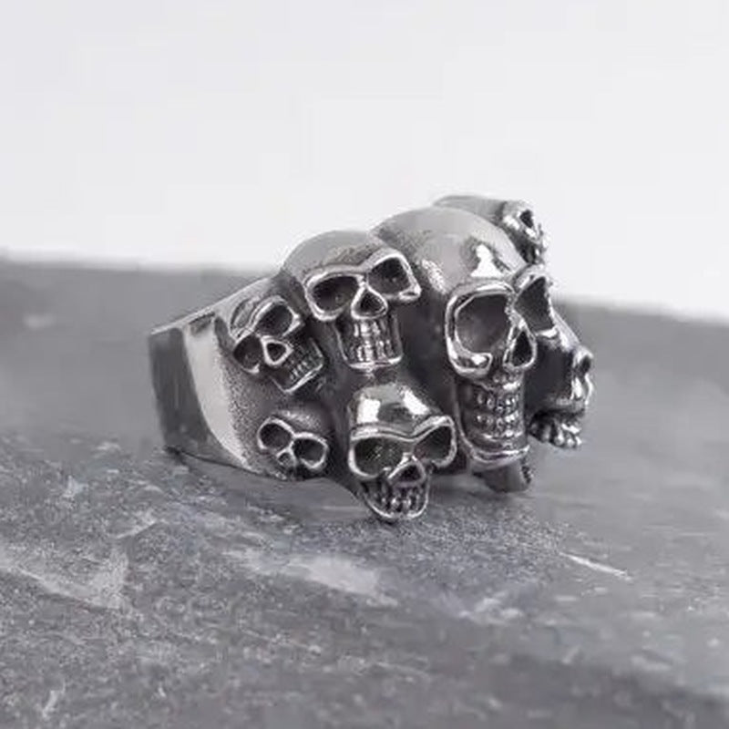 Silver skull ring with multiple cluster skulls, shown on dark stone surface | Chaps London