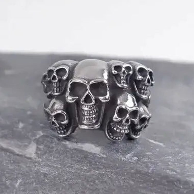 Silver skull ring with multiple skulls, shown flat on dark stone surface | Chaps London