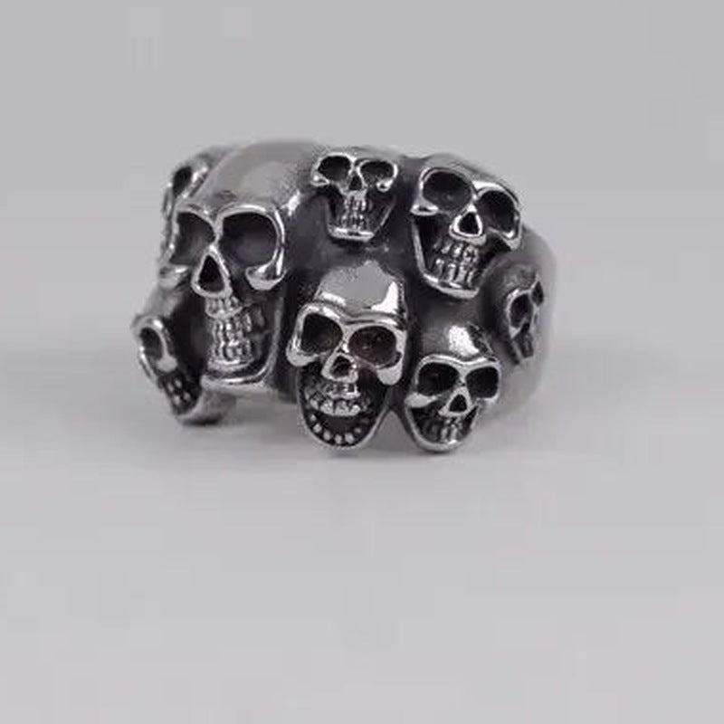 Silver-toned wide band ring with multiple skull faces, shown flat | Chaps London
