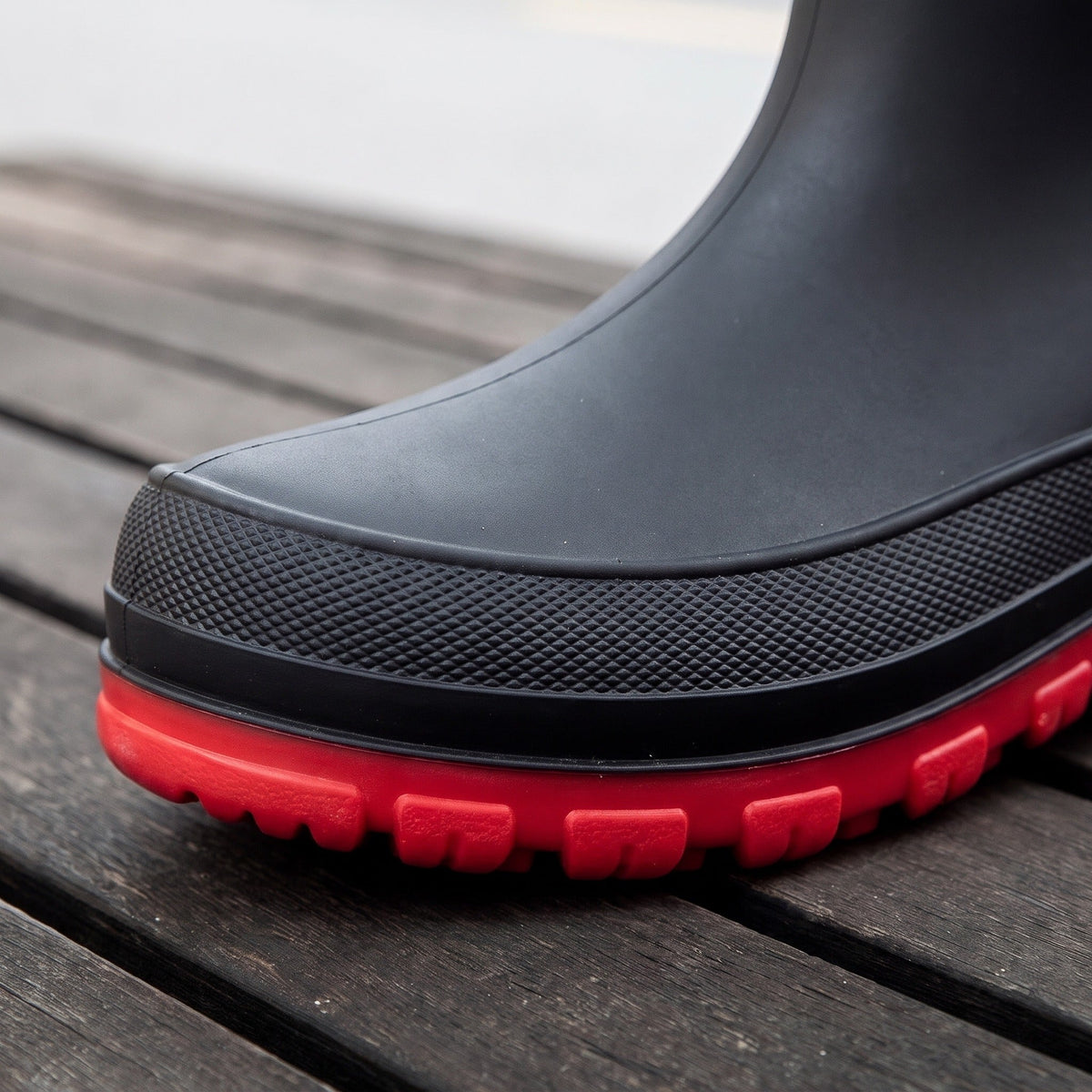 Close-up of black mid-calf welly toe with red textured sole, worn, outdoors | Chaps London