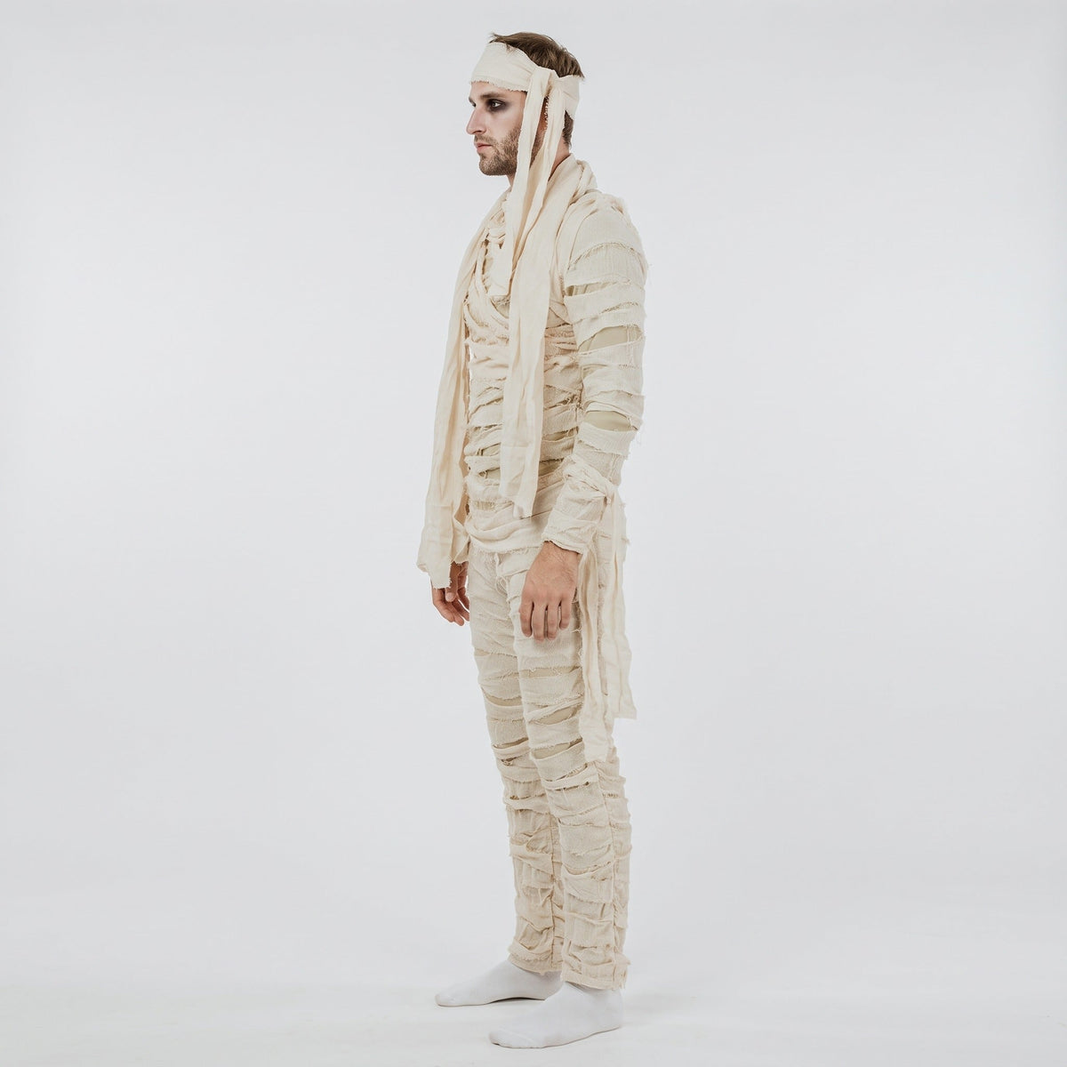 Man wearing cream mummy costume jumpsuit with frayed wraps and headband, side view | Chaps London