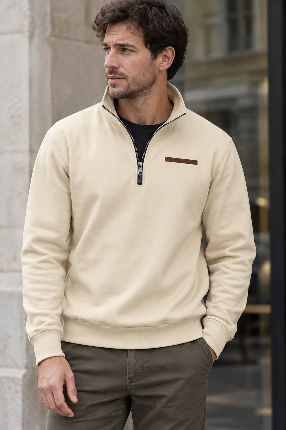 Man wearing a beige funnel neck sweatshirt open at the collar over a black T-shirt, one hand in his pocket | Chaps London