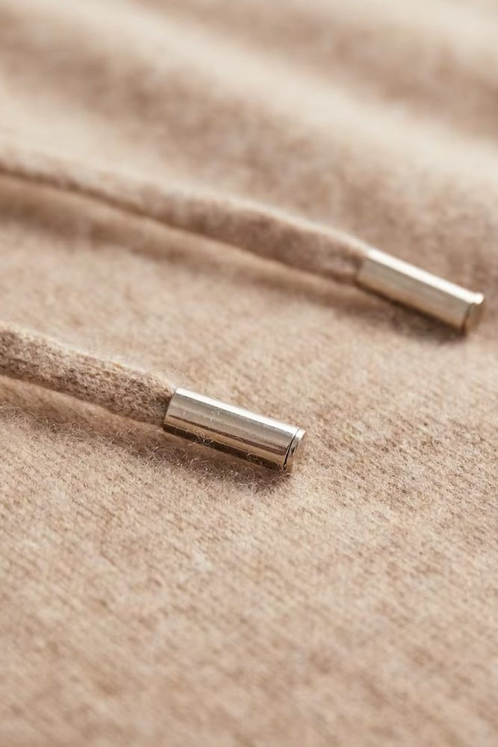 Men's knitted hooded jumper in beige, close-up of the metal tips of the drawstring