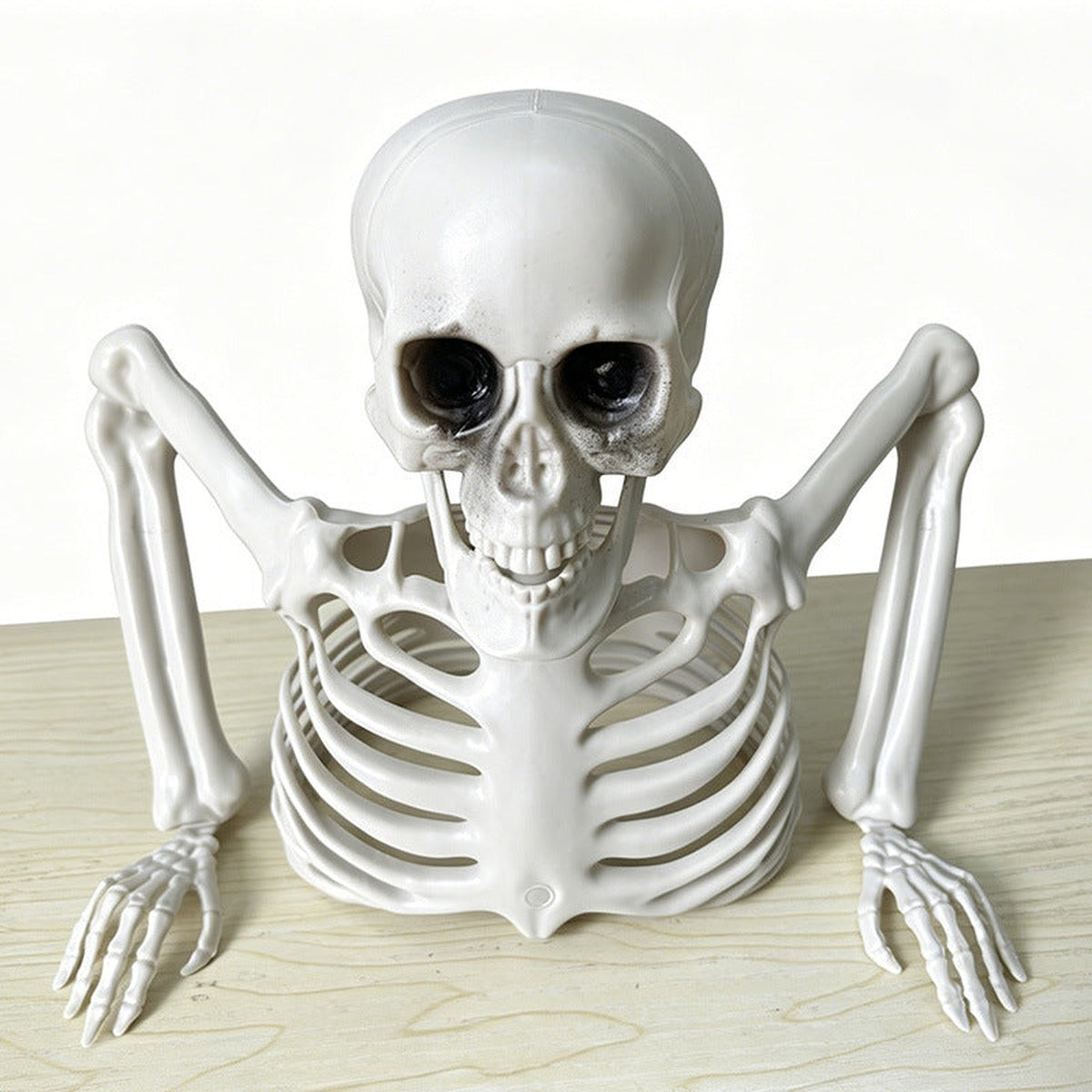 White plastic skeleton figure leaning forward, arms resting flat on table surface | Chaps London