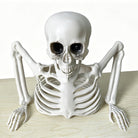 White plastic skeleton figure leaning forward, arms resting flat on table surface | Chaps London