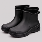 All black ankle rain boots with ribbed knit cuffs and black lugged soles on a grey studio background.