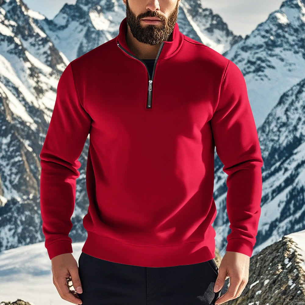 Man wearing a red quarter zip jumper open at the neck over a black T-shirt, snowy peaks behind him | Chaps London