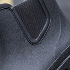 A pair of black rubber Chelsea style rain boots with elastic side panels and pull tabs standing on a street with yellow road markings, close-up view