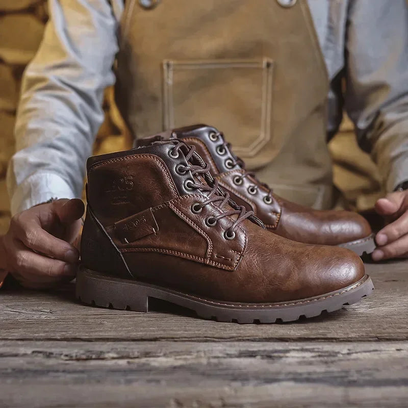 Brown faux leather lace-up ankle boots on wooden surface, person holding them | Chaps London