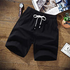 Black cotton drawstring shorts laid flat on wooden surface with accessories | Chaps London