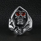 Silver hooded skull ring with red eyes, flat on dark surface | Chaps London