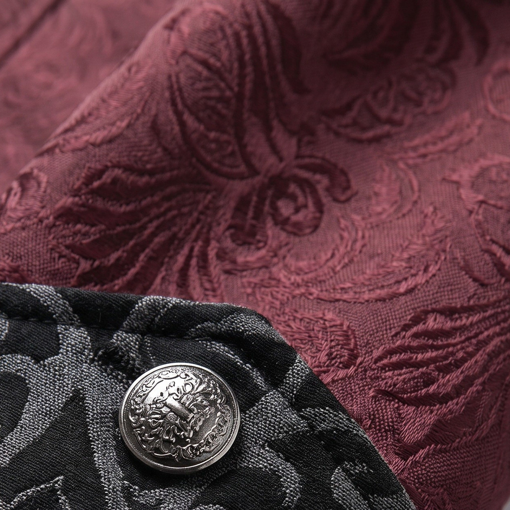 Burgundy jacquard fabric with ornate pattern beside black textured fabric and silver button | Chaps London