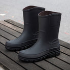 Black mid-calf rain boots with ridged soles, displayed on wooden bench | Chaps London