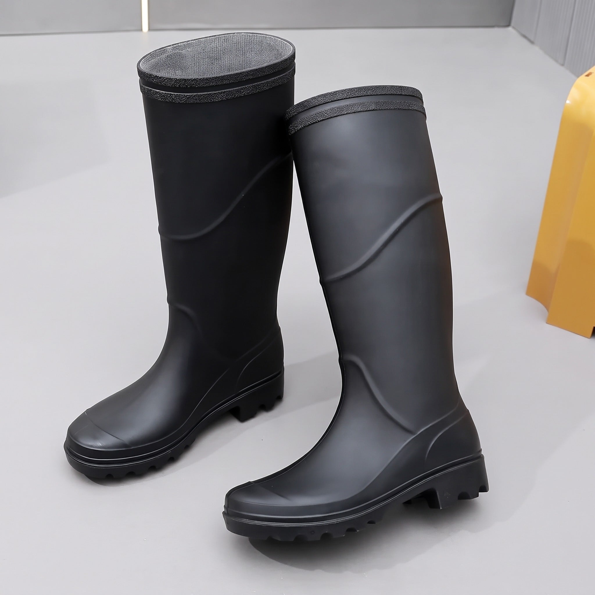 Black knee-high rubber boots with ridged soles, displayed standing on gray surface | Chaps London