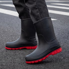 Black mid-calf wellies with red soles, worn by a person on pavement | Chaps London