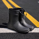 Black ankle Wellington boots with drawcord collar, standing on road surface | Chaps London
