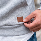 Grey hoodie worn by person, hand touching leather-look patch on hem | Chaps London