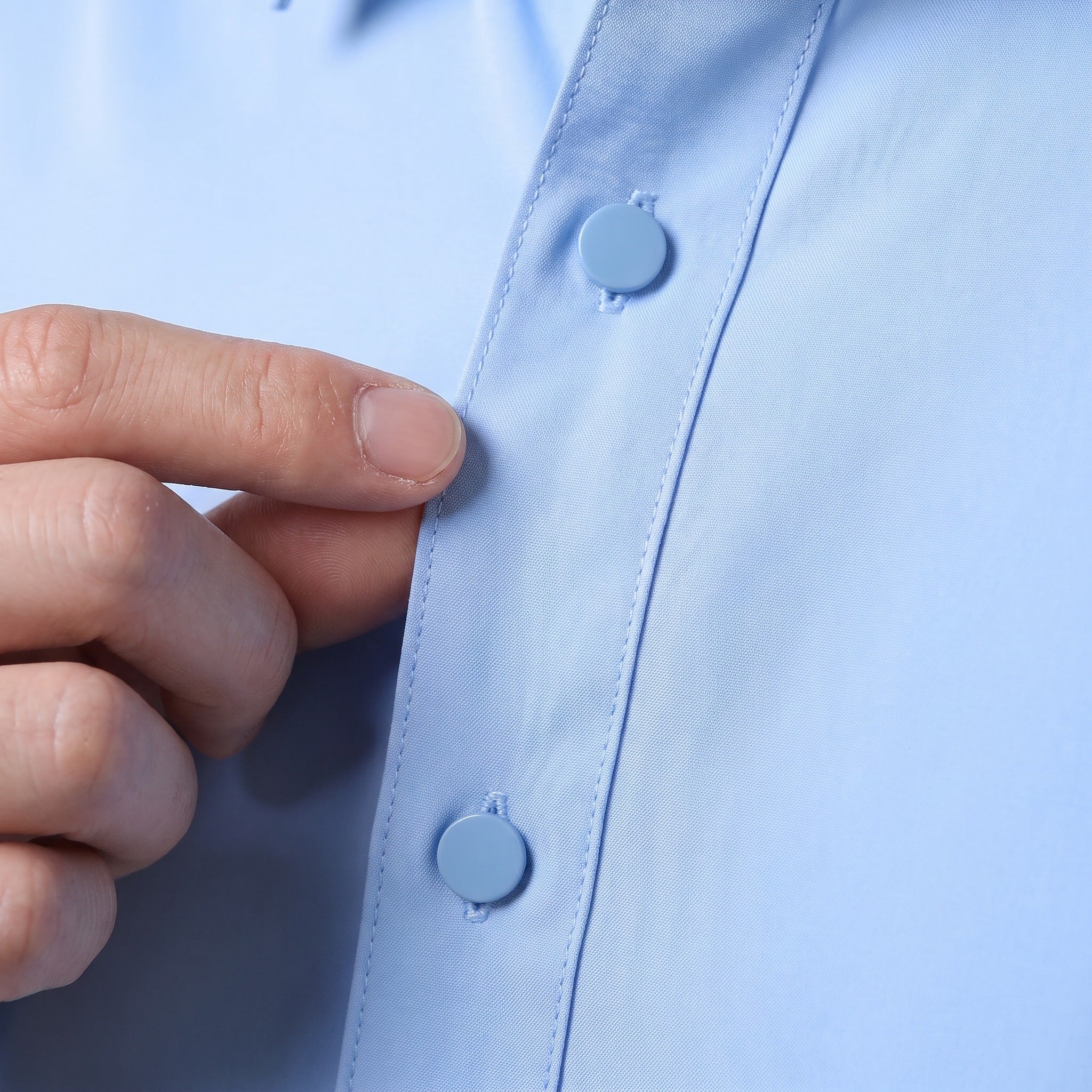 Close-up of hand buttoning light blue shirt placket, worn by person | Chaps London