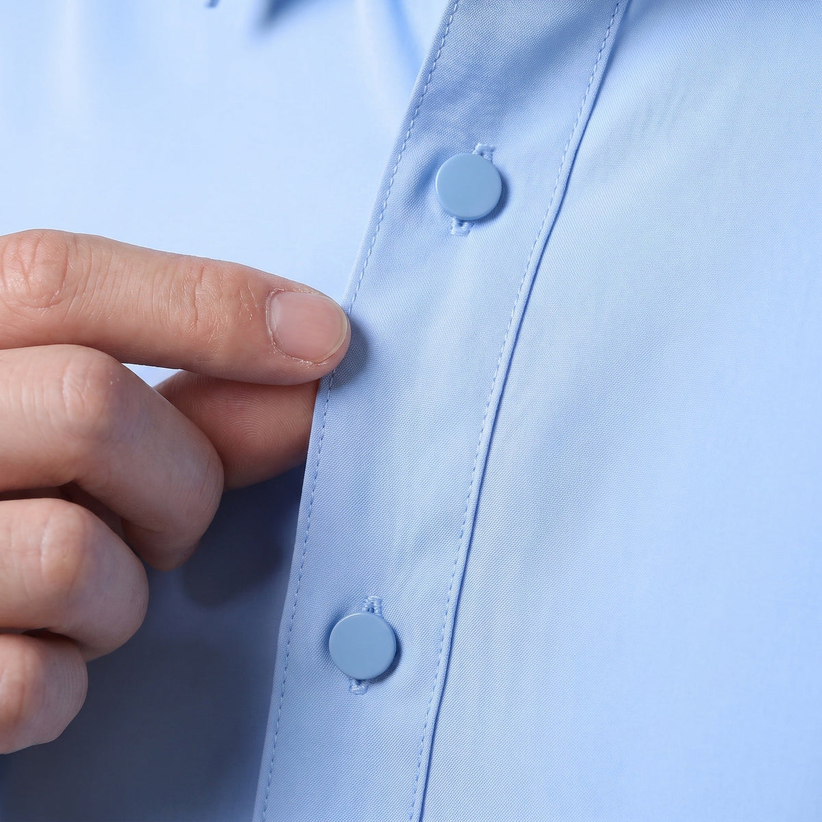 Close-up of hand buttoning light blue shirt placket, worn by person | Chaps London