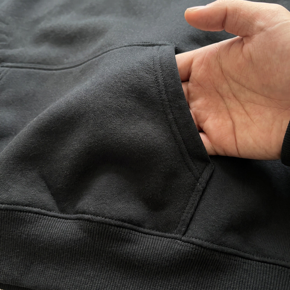 Close-up of black hoodie kangaroo pocket with hand reaching inside | Chaps London