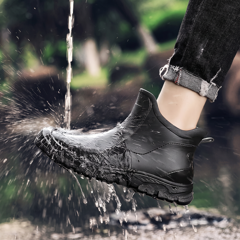 A black rain boot being splashed with a stream of water, worn on a leg with rolled black jeans.