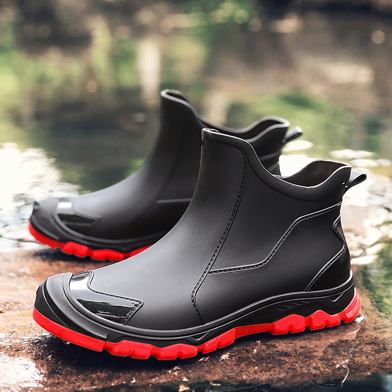 A pair of black ankle boots with red soles sits on a wet stone surface near water.