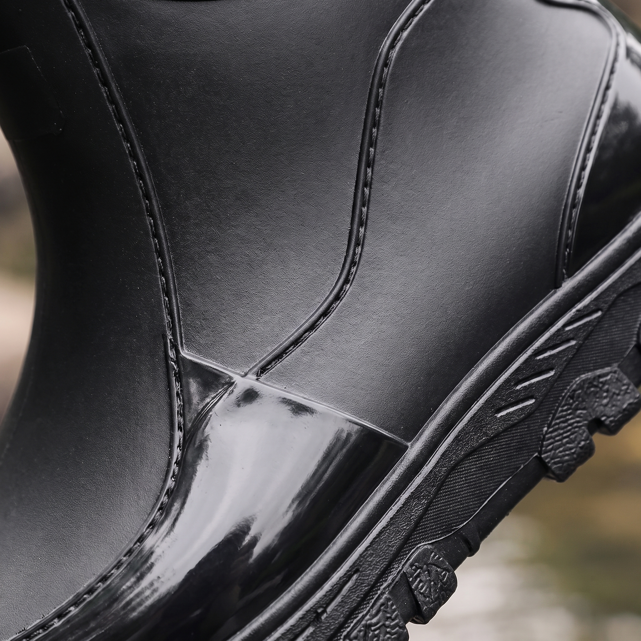 A black rain boot being splashed with a stream of water, worn on a leg with rolled black jeans, close-up view
