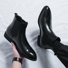 Black faux leather Chelsea boots, one worn, one held by hand | Chaps London