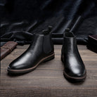Black leather Chelsea ankle boots with elastic side panels, displayed on wooden surface | Chaps London