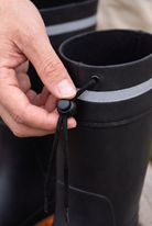 Close-up of the drawstring toggle and reflective band at the top of a black rain boot.