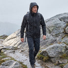 Man wearing black hooded rain jacket hiking on wet rocky trail | Chaps London