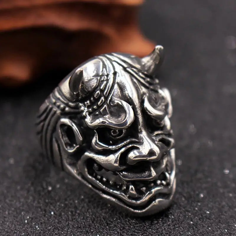 Silver-toned Oni demon mask ring with horns, shown flat on dark surface | Chaps London