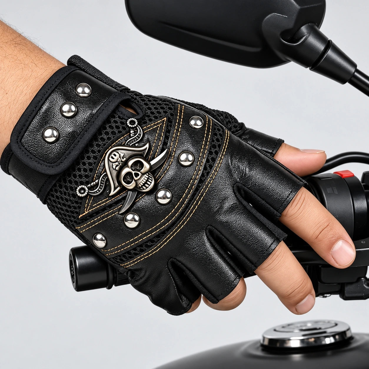 Black fingerless biker glove with skull emblem, rivets, worn on hand gripping handlebar | Chaps London