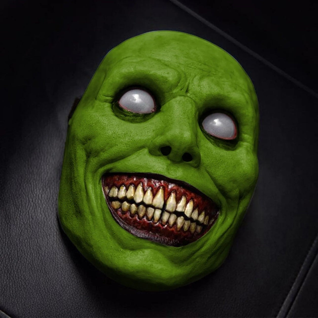 Green smiling demon mask with white eyes, shown flat on surface | Chaps London